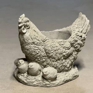 May include: A gray concrete planter shaped like a hen with three chicks. The hen has a detailed feathered texture and a small planter in her back.