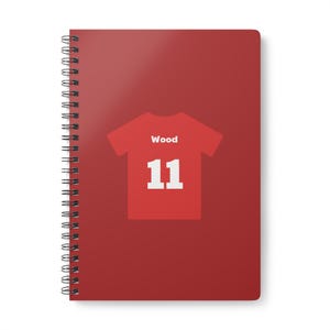 May include: Red spiral-bound notebook with a red t-shirt graphic. The t-shirt design includes the word "Wood" above the number "11" in white. The notebook's cover is a solid red color.