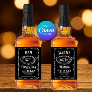 May include: Two glass whiskey bottles with black caps and amber liquid. The labels are black with white text and ornate borders. The left label reads DAD, The Best No. 1, Father's Day, WHISKEY, 15.06.2027. The right label reads JEREMY, Aged No. 40, Birthday, WHISKEY, 19.10.2026.