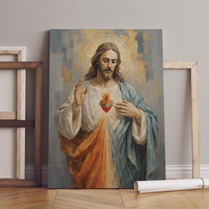 Op de afbeelding: Een religieus schilderij met een figuur met lang haar, gekleed in witte en blauwe gewaden, en een rood hart met vlammen. Het kunstwerk heeft een halo en staat tegen een zachte, getextureerde achtergrond. Het schilderij leunt tegen een muur.