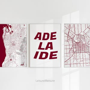 May include: Three framed prints with a white background. The centre print features the word "ADELAIDE" in bold, red letters. The prints on either side feature a map of Adelaide, Australia, with red lines on a white background.