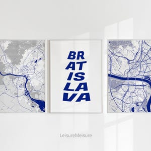 May include: Three framed prints, one with a map of Bratislava, one with the text "BRATISLAVA" in blue letters, and one with a map of Bratislava. The prints are on a white wall.
