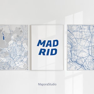 Op de afbeelding: Drie ingelijste prints aan een witte muur. Twee prints tonen blauwe stadskaarten en de centrale print toont het woord "MADRID" in vette blauwe letters. De prints worden weergegeven op een witte muur.
