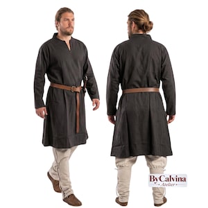 Op de afbeelding: Een donker antracietkleurige tuniek met lange mouwen en een V-hals, gecombineerd met een bruine leren riem en een lichtbeige broek. Het ensemble wordt van voor- en achterkant getoond, met een eenvoudig ontwerp en het ByCalvina Atelier logo.
