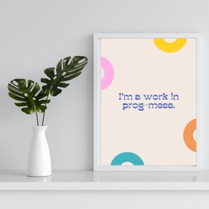 Può includere: Una stampa incorniciata bianca con uno sfondo beige e cerchi colorati. Il testo sulla stampa recita "I'm a work in prog-mess."