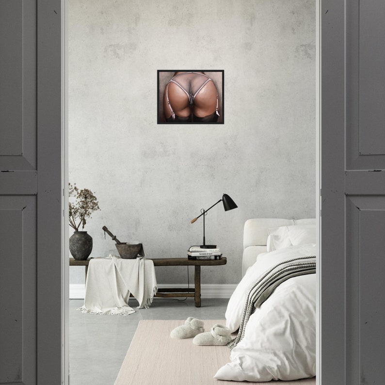 Op de afbeelding: Een ingelijste print met een close-up van de billen van een persoon in doorschijnend lingerie. De lingerie is licht van kleur met jarretelles. De afbeelding wordt weergegeven op een lichtgrijze muur in een slaapkamer.