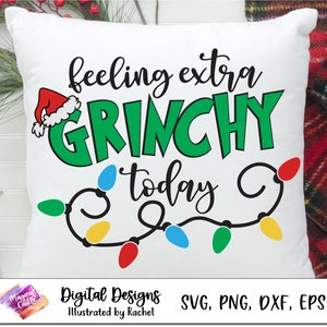 May include: White pillow with green text that reads "feeling extra GRINCHY today" with a red and white Santa hat and a string of colorful lights.