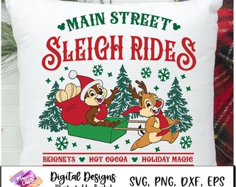 May include: A white pillow with a red and green Christmas design featuring Chip and Dale riding a sleigh. The text "Main Street Sleigh Rides" is in red and green. The text "Beignets Hot Cocoa Holiday Magic" is in red and green. The text "Digital Designs Illustrated by Rachel SVG, PNG, DXF, EPS" is in black and white.
