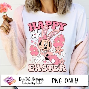 Puede incluir: Una camiseta blanca con un gráfico rosa y blanco de un ratón de dibujos animados con orejas de conejo y sosteniendo un huevo de Pascua. El gráfico dice "Feliz Pascua" en letras rosas.