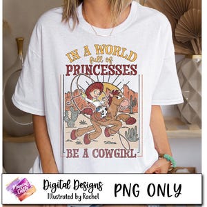 May include: A white t-shirt with a vintage-style graphic featuring a cartoon cowgirl riding a horse. The text reads "In a world full of princesses, be a cowgirl".
