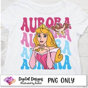 Może przedstawiać: Biały T-shirt z r&oacute;żowym, niebieskim i jasnoniebieskim wzorem graficznym przedstawiającym księżniczkę Disneya Aurorę, znaną r&oacute;wnież jako Śpiąca Kr&oacute;lewna, z tekstem "AURORA" powt&oacute;rzonym w retro czcionce. Grafika zawiera r&oacute;wnież mały obrazek przyjaciela sowy Aurory, w prawym g&oacute;rnym rogu.