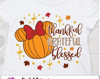 May include: A white t-shirt with a design featuring a pumpkin-shaped Minnie Mouse head with a red bow, surrounded by gold stars and fall leaves. The text "thankful grateful blessed" is written in a brown script font.