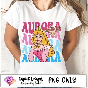 Może przedstawiać: Biały t-shirt z r&oacute;żowym, niebieskim i jasnoniebieskim wzorem graficznym z napisem "Aurora" powt&oacute;rzonym cztery razy. Grafika zawiera r&oacute;wnież kresk&oacute;wkową postać księżniczki Aurory ze Śpiącej Kr&oacute;lewny i małą sowę.