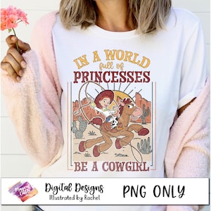 May include: A white t-shirt with a vintage-style graphic featuring a cartoon cowgirl riding a horse. The text reads "In a world full of princesses, be a cowgirl".