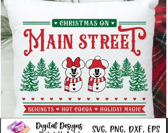 Könnte beinhalten: Ein weißes Kissen mit einem roten und grünen Weihnachtsmotiv. Der Text "Christmas on Main Street" ist in Rot mit grünen Akzenten. Das Design enthält auch zwei Schneemänner, einer mit einer roten Schleife und der andere mit einer roten Weihnachtsmütze. Der Text "Beignets Hot Cocoa Holiday Magic" ist in Rot mit grünen Akzenten.