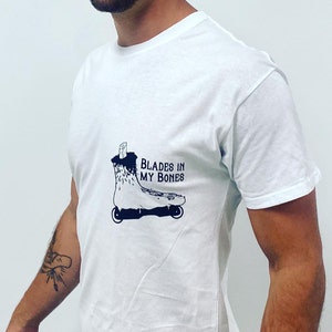Può includere: Maglietta bianca con un'illustrazione in bianco e nero di un pattino a rotelle con il testo "BLADES IN MY BONES".
