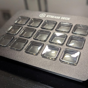 May include: A black Stream Deck with 15 customizable buttons. Each button has a clear, square, plastic cover.