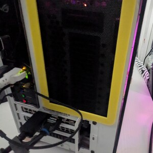 May include: A white computer case with a yellow frame around a black mesh panel. The panel has a row of pink lights behind it. The case is sitting on a white surface.