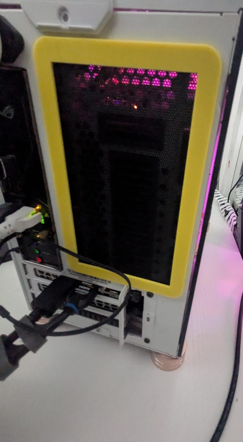 May include: A white computer case with a yellow frame around a black mesh panel. The panel has a row of pink lights behind it. The case is sitting on a white surface.