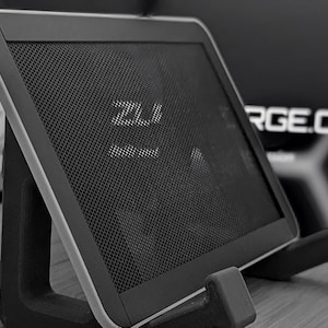 May include: A black and gray tablet-like device with a mesh screen, resting on a black stand. The device has a silver trim and the text "ZLI" is visible on the screen. The stand has two supporting arms.