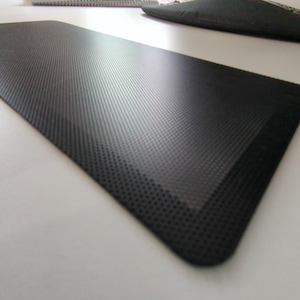 Peut inclure: Tapis anti-fatigue noir avec une surface texturée. Le tapis est conçu pour offrir confort et soutien lors de longues périodes debout.