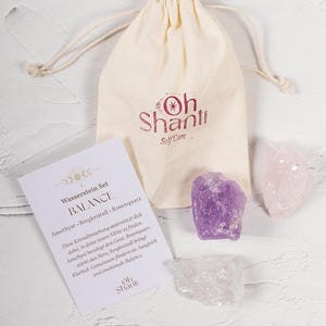 Könnte beinhalten: Ein Self-Care-Set mit einem Kordelzugbeutel mit der Aufschrift "Oh Shanti Self Care", einer Karte und drei Kristallen. Die Kristalle sind Amethyst, Rosenquarz und Bergkristall. Die Karte hat Text auf Deutsch.