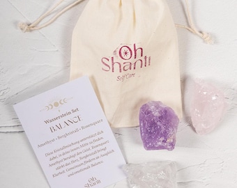 Könnte beinhalten: Ein Self-Care-Set mit einem Kordelzugbeutel mit der Aufschrift "Oh Shanti Self Care", einer Karte und drei Kristallen. Die Kristalle sind Amethyst, Rosenquarz und Bergkristall. Die Karte hat Text auf Deutsch.