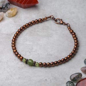 May include: A copper beaded bracelet with a green stone accent. The bracelet has a lobster clasp closure.