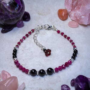 May include: A silver bracelet featuring black and pink beads. The bracelet has a silver clasp and a small pink flower charm.