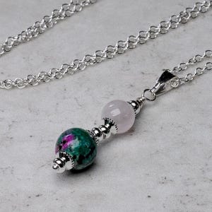 May include: A silver chain necklace with a pendant featuring two round gemstone beads. The larger bead is pink and the smaller bead is green with pink and white flecks.