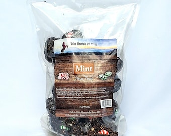 以下が含まれることがあります： ミント味のダークブラウンの馬用おやつが入った袋。袋には「Welsh Mountain Pet Treats」と「Mint Horse Treat」のラベルが貼られています。おやつは小さく丸いボールの形をしていて、中には赤と白のキャンディーケーンが入っています。袋は3ポンドです。