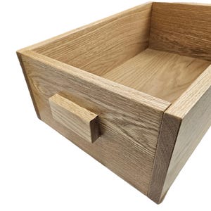 May include: A wooden box with a natural finish and a simple rectangular handle. The box is made of solid wood and has a smooth, polished surface.