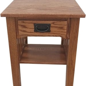 May include: A wooden end table with a single drawer and a lower shelf. The drawer has a black metal pull handle. The table is made of a light brown wood.