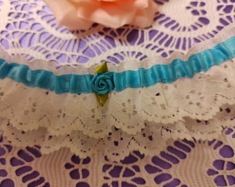Könnte beinhalten: Weißes Spitzen-Strumpfband mit einem blauen Satinband und einem grün-weißen Blumenakzent.