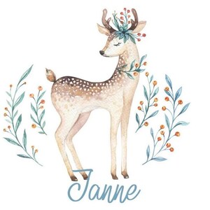 Könnte beinhalten: Aquarell-Illustration eines Rehs mit einer Blumenkrone, umgeben von grünen Zweigen mit orangefarbenen Beeren. Der Name "Janne" ist in blauer Schrift unter dem Reh geschrieben.
