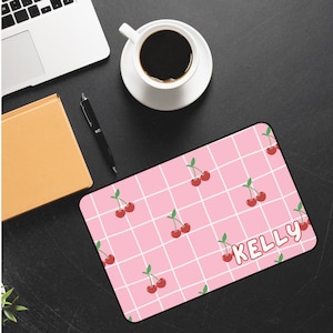 May include: Pink and white checkered mousepad with a repeating pattern of red cherries. The text "KELLY" is printed in white on the mousepad.