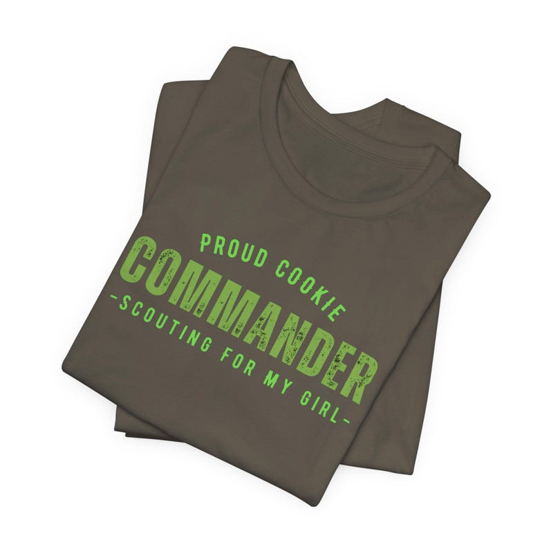 Może przedstawiać: Brązowa koszulka z napisem "Proud Cookie Commander - Scouting for my girl -" w kolorze zielonym.