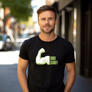 Puede incluir: Una camiseta negra con un gr&aacute;fico verde de un b&iacute;ceps flexionado con el texto "Cookie Security" en &eacute;l.