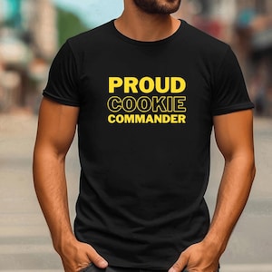 May include: A black t-shirt with the text "PROUD COOKIE COMMANDER" in yellow letters.