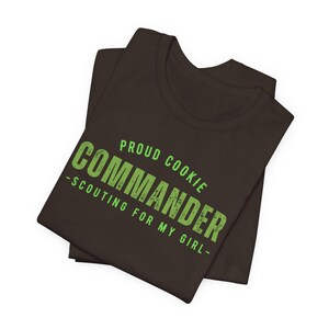 Może przedstawiać: Ciemnobrązowy t-shirt z napisem "Proud Cookie Commander - Scouting for my girl -" w kolorze zielonym.
