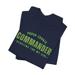 Może przedstawiać: Koszulka w kolorze granatowym z napisem "Proud Cookie Commander - Scouting for my girl -" w kolorze zielonym.