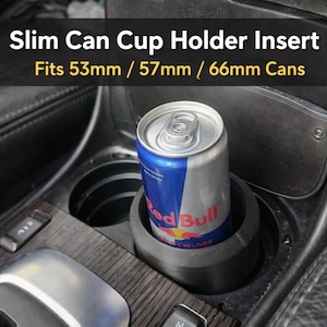 May include: Black cup holder insert designed for slim cans, fitting 53mm, 57mm, and 66mm cans. A Red Bull can is placed inside the holder, demonstrating its use. The text "Slim Can Cup Holder Insert" is visible.
