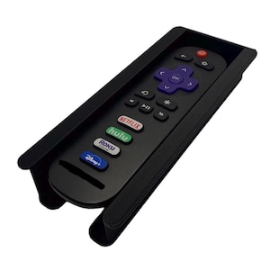Puede incluir: Soporte negro para mando a distancia con un mando Roku en su interior. El mando tiene botones para Netflix, Hulu y Disney+. El soporte tiene una superficie texturizada y está diseñado para sujetar el mando de forma segura.