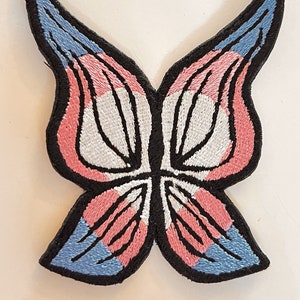 May include: A blue, pink, and white butterfly embroidered patch. The butterfly is outlined in black thread.