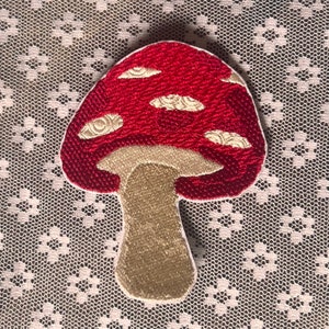 Peut inclure: Patch brodé en forme de champignon rouge et blanc avec un pied beige.