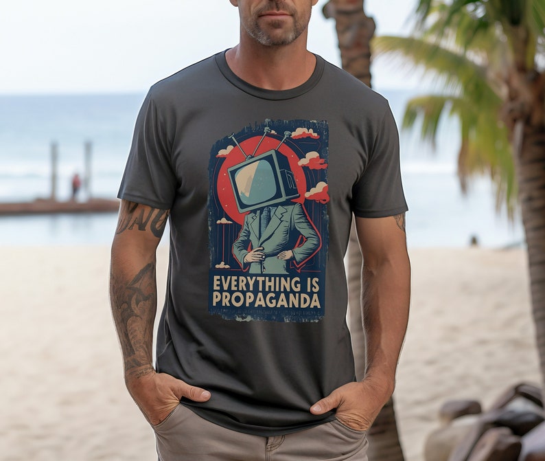 May include: A dark gray t-shirt with a vintage-style graphic of a television with a human body and the text "Everything is Propaganda".