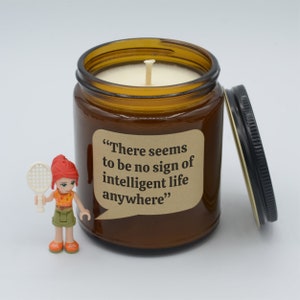 May include: A brown glass candle jar with a black lid. The candle jar has a label with the text "There seems to be no sign of intelligent life anywhere".