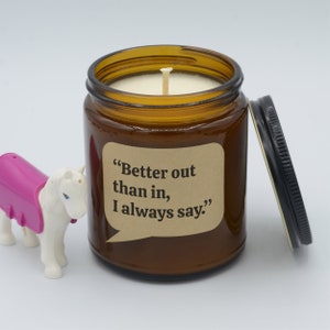 May include: A brown glass candle jar with a white candle and a brown paper label with the text "Better out than in, I always say."