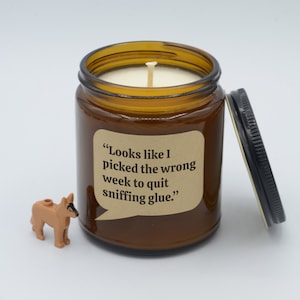 May include: A brown glass candle jar with a white candle inside. The jar has a label that reads "Looks like I picked the wrong week to quit sniffing glue."