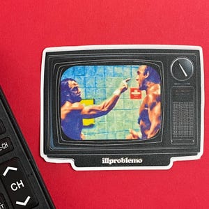 May include: A sticker featuring a retro television displaying a colorful image of two muscular men. One man points at the other. The sticker has a white border and the text "illproblemo" at the bottom. A black remote control is in the corner.